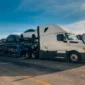 White semi-truck pulling a fully loaded car hauler trailer with secured vehicles ready for safe auto transport