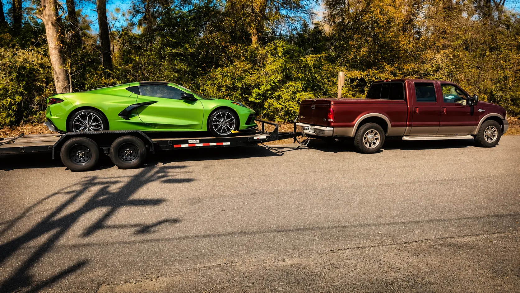 A deep red heavy-duty pickup truck securely towing a bright green sports car on a flatbed trailer, demonstrating reliable auto transport by Your Xpert Trans.